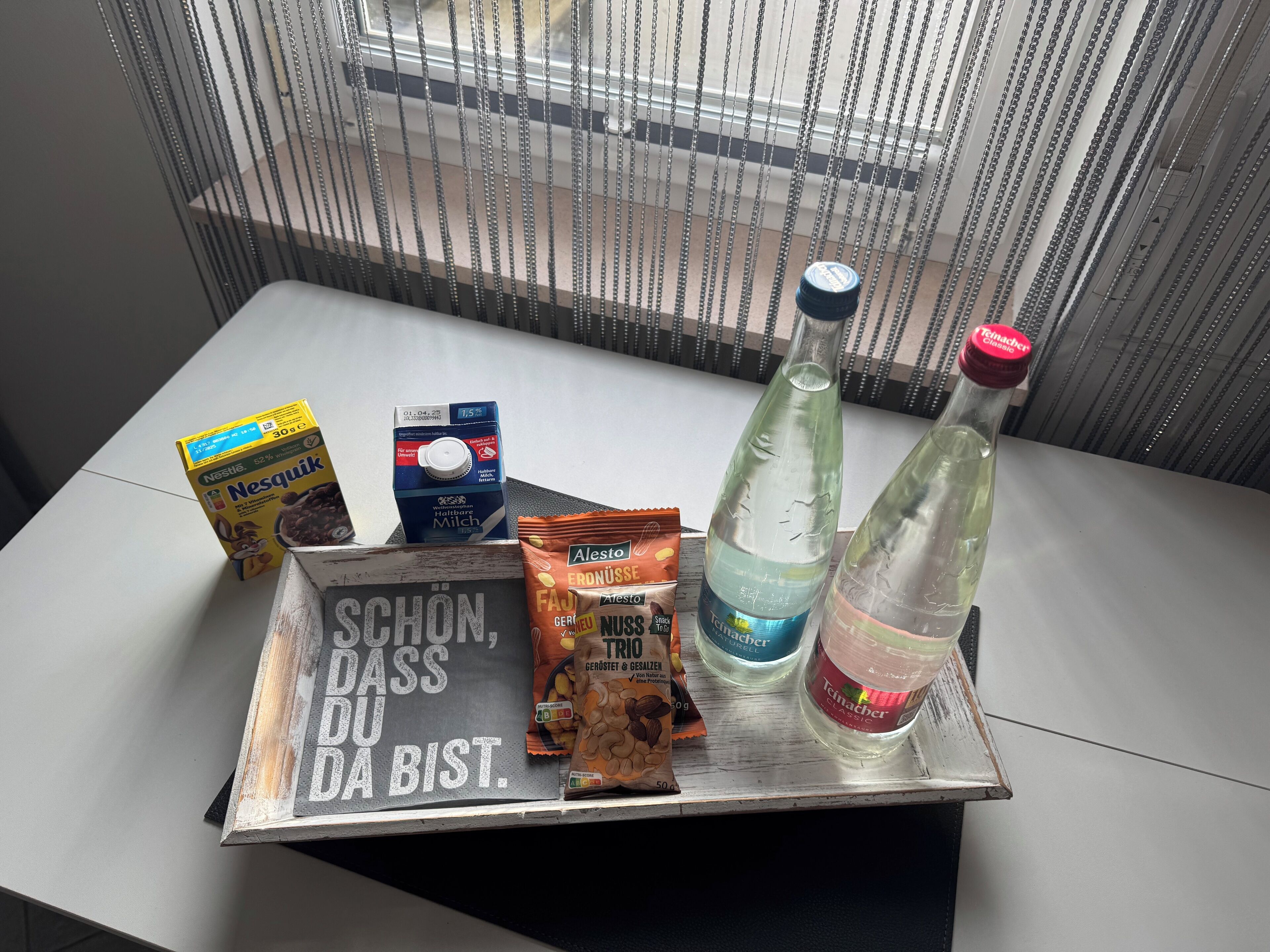 En bakke med en karton Nestlé mælk, en vandflaske, en flaske Teimacher Classic, en pakke Trigo, og et skilt med tysk tekst.