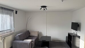 Ein modernes Wohnzimmer mit grauem Sofa, einem schwarzen Couchtisch, einem schwarzen TV-Schrank und einer Heizung.
