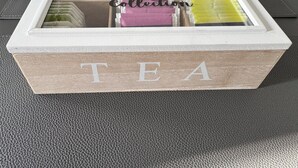 Eine Holzkiste mit dem Schriftzug "TEA", gefüllt mit verschiedenen Teebeuteln.