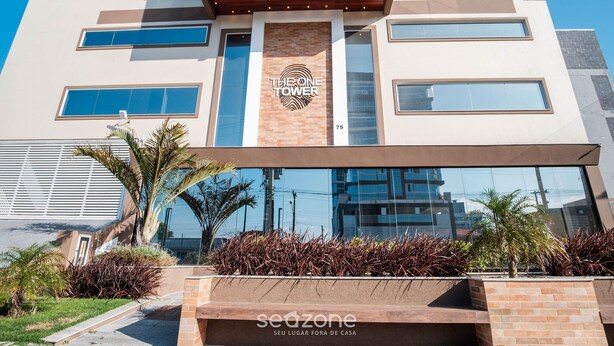 A modern building with a sign reading "THE ONE FOWER" and a logo. It features a large glass facade, a brick base, and a landscaped area with plants. - Studio in a Condo w/ Pool 550m From Beach Tor0407 (Imbituba)
