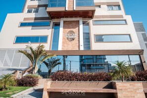 A modern building with a sign reading "THE ONE FOWER" and a logo. It features a large glass facade, a brick base, and a landscaped area with plants. - Studio in a Condo w/ Pool 550m From Beach Tor0407 (Imbituba)
