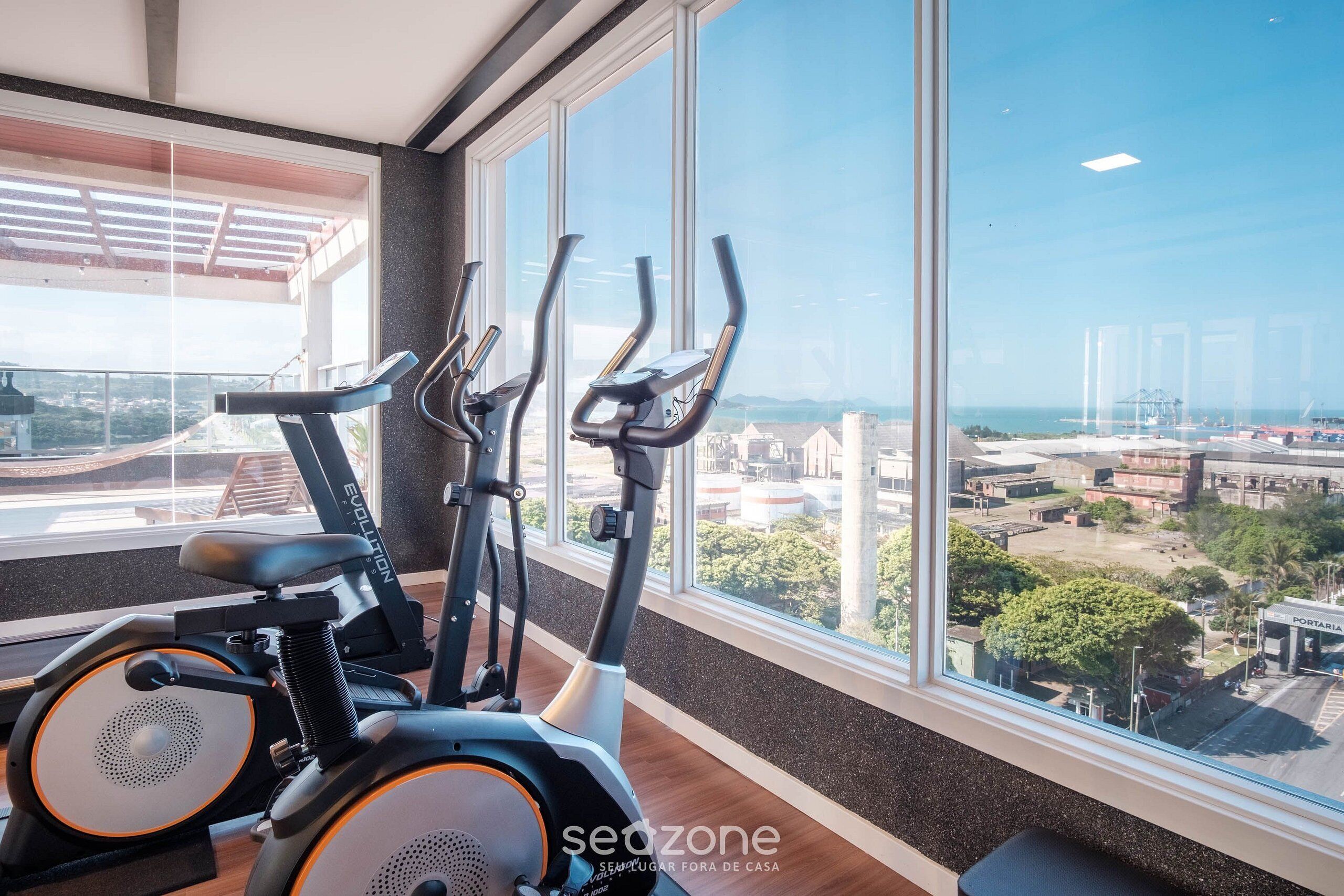 Un gimnasio interior con bicicletas estáticas y vistas a la ciudad a través de amplios ventanales.
