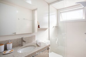 A modern bathroom with a granite countertop, a white sink, a glass shower enclosure, and a large mirror. - Studio in a Condo w/ Pool 550m From Beach Tor0407 (Imbituba)