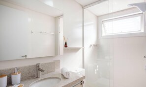 Casa de banho moderna com bancada de granito, lavatório branco, cabine de duche em vidro e um espelho grande.