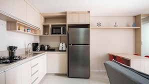 A modern kitchen with a built-in stainless steel refrigerator, a microwave, and a coffee maker. There are wooden cabinets and a small shelf with kitchen items. - Studio in a Condo w/ Pool 550m From Beach Tor0407 (Imbituba)