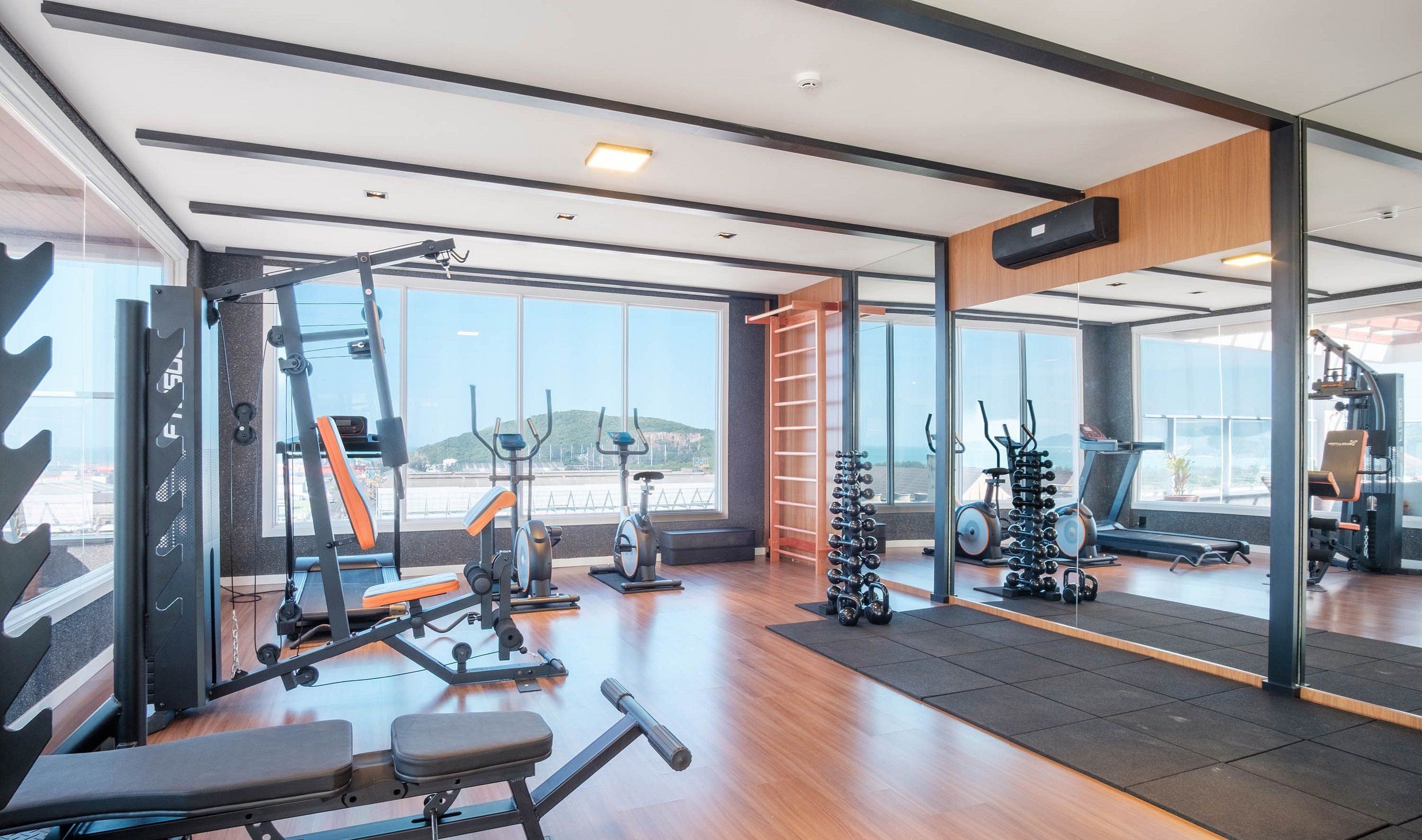 Un gimnasio moderno con varios equipos de ejercicio, ventanas amplias y vistas al exterior.