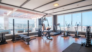 A gym with various exercise equipment, large windows offering a view of the city, and a wooden floor. - Studio in a Condo w/ Pool 550m From Beach Tor0407 (Imbituba)