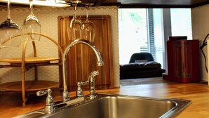 A kitchen with a stainless steel sink, wooden cabinets, and a shelf with glassware and dishes. - Copper Den Condo by the Bay, Chic & Cozy studio (Daphne)