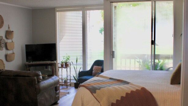 A bedroom with a bed, a sofa, a television, and a sliding glass door leading to a balcony. - Copper Den Condo by the Bay, Chic & Cozy studio (Daphne)