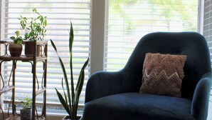 A dark blue armchair with a patterned pillow, a wooden floor, and a window with blinds. - Copper Den Condo by the Bay, Chic & Cozy studio (Daphne)