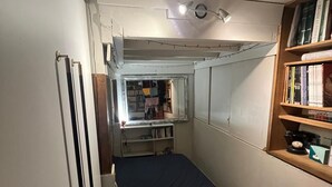 A compact bedroom with a bed, a red dresser, a bookshelf, and a window with a view of a room containing a desk and shelves. - Cozy studio (Paris)