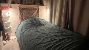 A bedroom with a bed, a shelf with personal items, a desk with a lamp, and a window with curtains. - Cozy studio (Paris)