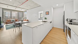 A modern kitchen with a central island, a dining area with a sofa and chairs, and a view of the cityscape through large windows. - Bright 2-bed Apartment With Gym, BBQ & Pool Access (Canberra)