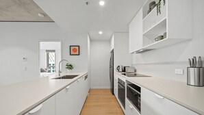 A modern kitchen with white cabinetry, a wooden floor, and a stainless steel refrigerator. - Bright 2-bed Apartment With Gym, BBQ & Pool Access (Canberra)