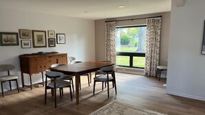 Un coin repas comprenant une table et des chaises en bois, un buffet en bois et une grande fenêtre avec des rideaux.