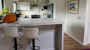 Une cuisine moderne avec des meubles blancs, un îlot central doté de deux tabourets de bar, des appareils en acier inoxydable et un éclairage suspendu.