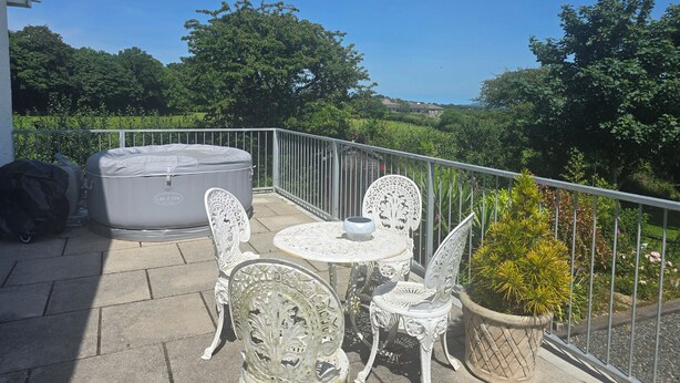 A balcony with a hot tub, white metal chairs, a small round table, and a potted plant.