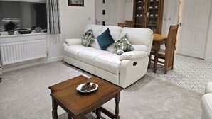 A living room with a white sofa, a wooden coffee table, and a dining table with chairs.