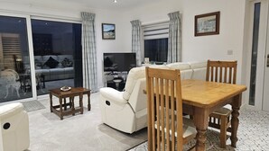 A living room with a sofa, a wooden dining table, a TV, and a balcony with curtains.