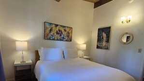 Een slaapkamer met een groot bed, twee nachtkastjes met lampen, een schilderij, een spiegel en houten balken in het plafond.
