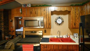 Una cocina con armarios de madera, un microondas, una estufa, un fregadero y un reloj en la pared.