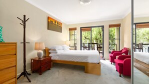 Un dormitorio con cama, mesita de noche, lámpara, perchero y ventana con vista a árboles.