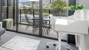 A modern room with a white desk, a patterned rug, and a view of buildings through large windows. - Modern 3-bedroom Townhouse in Quiet Greenway (Canberra)