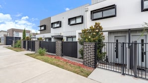 A modern residential building with a concrete driveway, black metal fence, and a small tree in the front yard. - Modern 3-bedroom Townhouse in Quiet Greenway (Canberra)