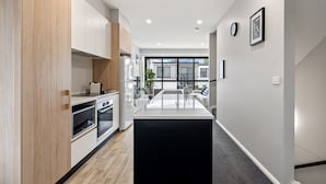 A modern kitchen with built-in appliances, a central island, and a view to the living area. - Modern 3-bedroom Townhouse in Quiet Greenway (Canberra)