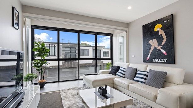 A modern living room with a white sofa, a coffee table, and a large window offering a view of buildings. - Modern 3-bedroom Townhouse in Quiet Greenway (Canberra)