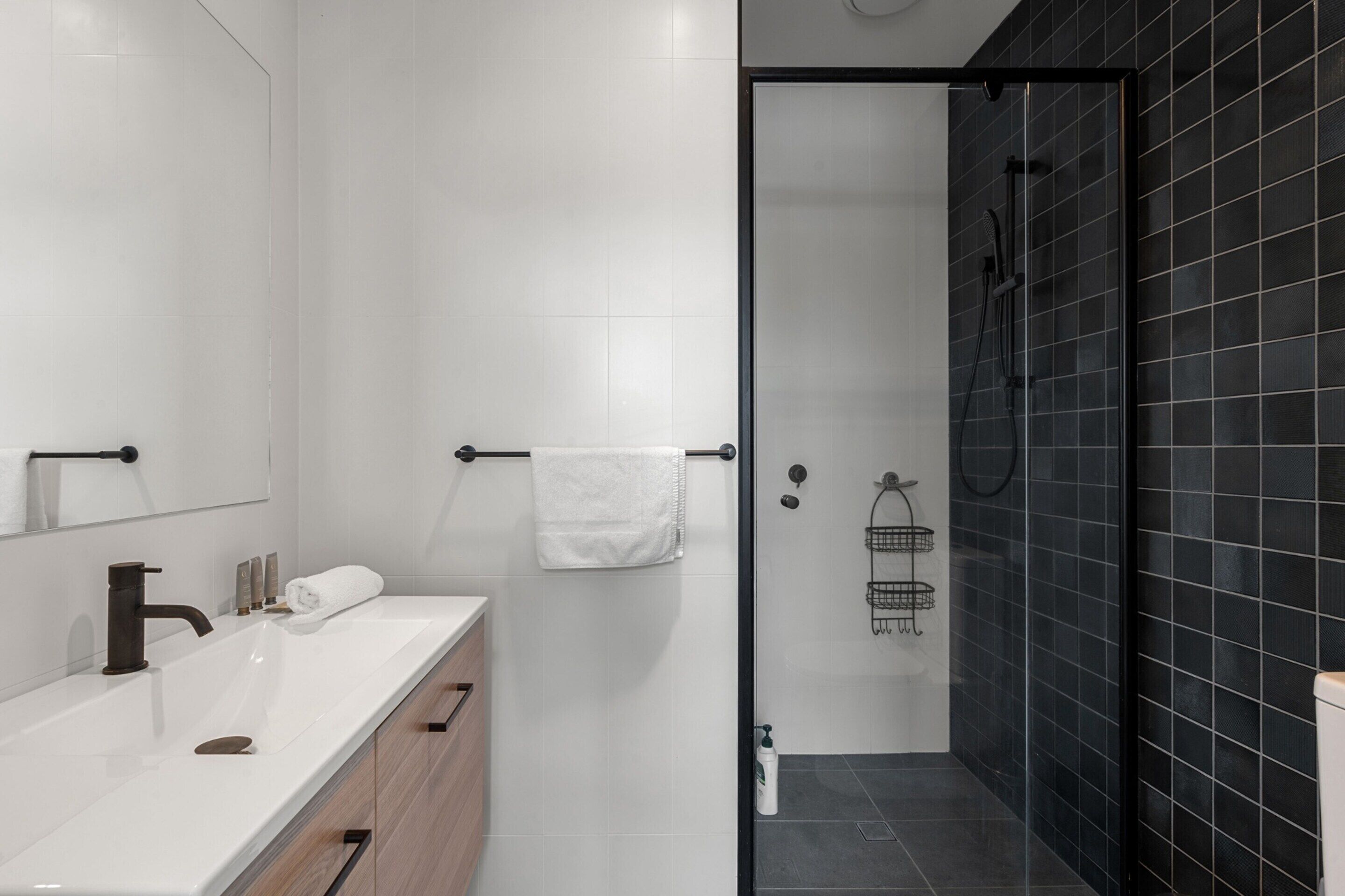 A modern bathroom with a white vanity, a glass-enclosed shower, and black tiled walls.