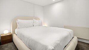 Un dormitorio moderno con cama, mesita de noche y luz empotrada en la pared.