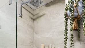 A shower area with a glass door, a showerhead, and a shelf with toiletries. - Chic Urban Paddington Escape (Sydney)