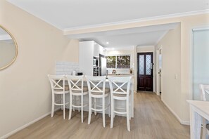 A modern kitchen with white cabinets, a dining area with white chairs, and a wooden floor.