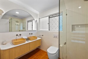 A modern bathroom with a glass shower enclosure, a wooden vanity with two sinks, and a white toilet.