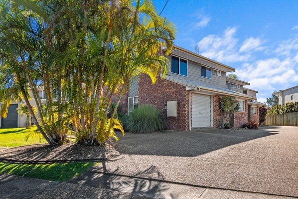 A two-story house with a garage, surrounded by a well-maintained lawn and palm trees.