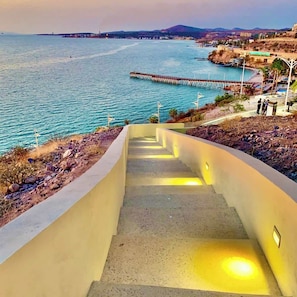 A concrete staircase leading down to a beach with a pier in the background.