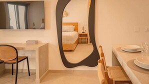 A modern hotel room with a large mirror, a bed, a desk, and a dining area.