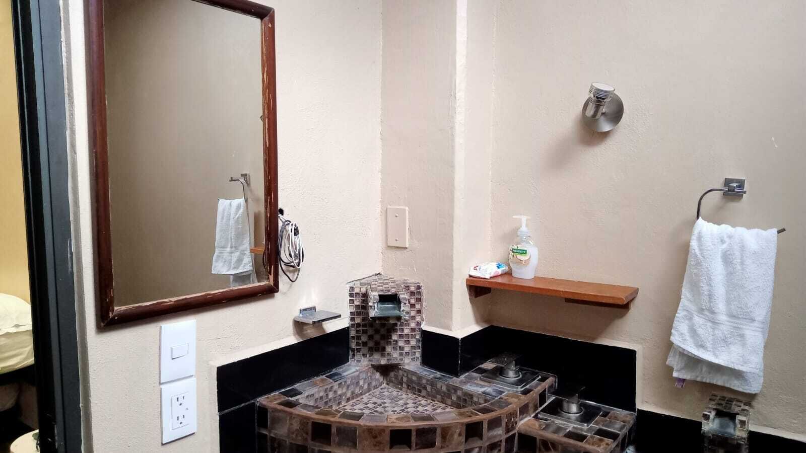 Ein Badezimmer mit Fliesenwaschbecken, einem Spiegel, einem Handtuchhalter und einem Ablagefach mit Toilettenartikeln.