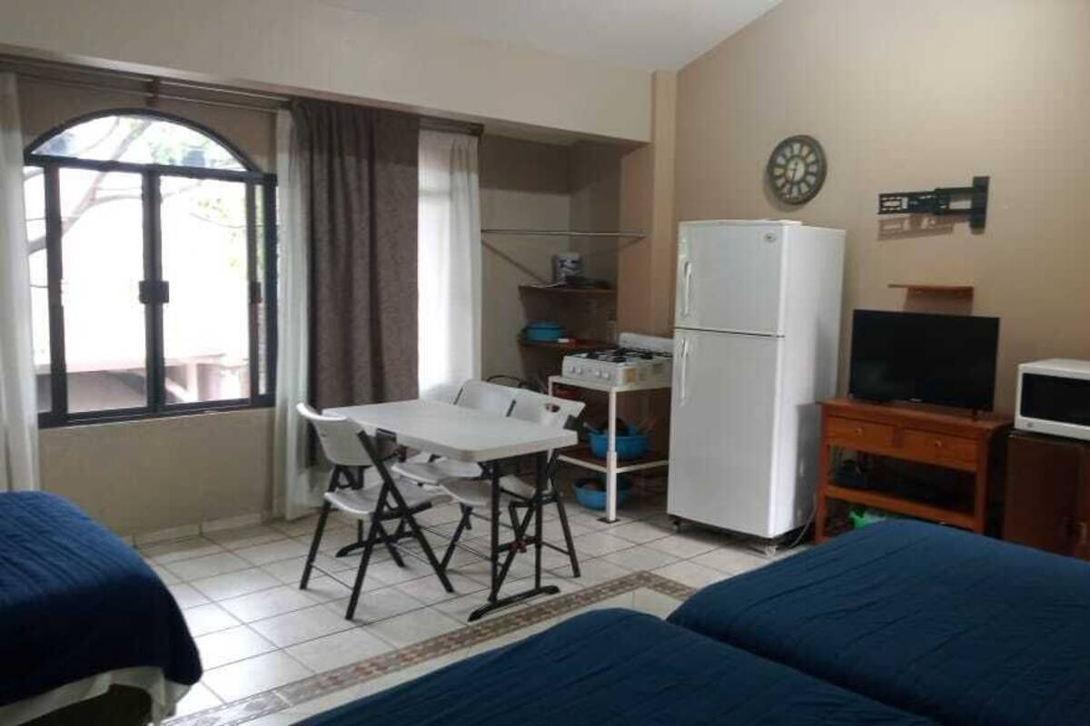 A room with two beds, a desk, a refrigerator, a television, and a window with curtains.