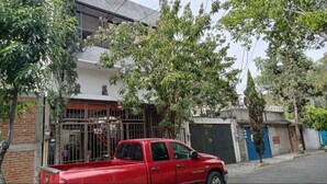 Una camioneta roja estacionada frente a un edificio con entrada vigilada y una puerta azul.