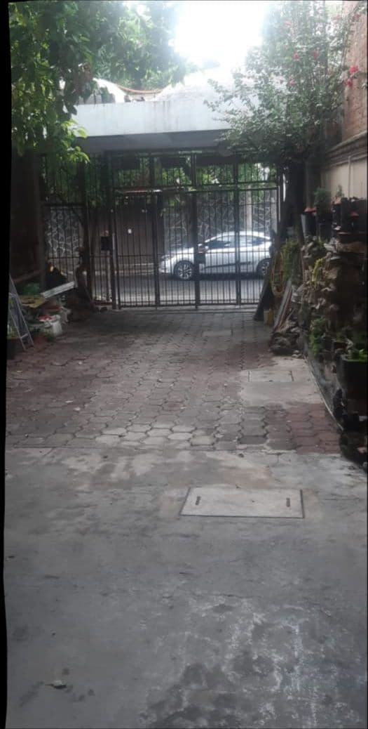 A gated courtyard with a paved path leading to a white car parked inside.