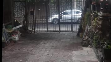 A gated courtyard with a paved path leading to a white car parked inside.