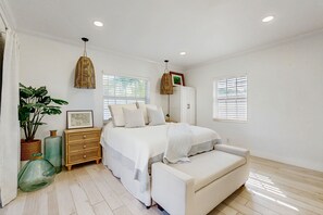 A bedroom with a bed, bedside tables, a dresser, a hanging light fixture, and a window with blinds. - Tropical backyard oasis w/ putting green, grill, tiki bar & walk to beach (Pompano Beach)