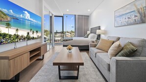 A modern hotel room with a large bed, a sofa, a wooden coffee table, and a painting of a beach scene. - Bright Studio in Trendy North Fremantle (Perth)