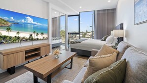 A modern hotel room with a large TV, a bed, a sofa, and a view of the beach. - Bright Studio in Trendy North Fremantle (Perth)