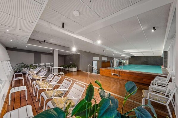 A modern indoor pool area with lounge chairs and a wooden deck.