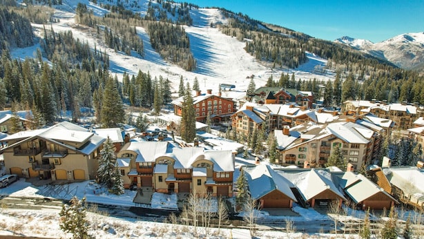 Un complejo turístico cubierto de nieve, con varios edificios, incluida una cabaña grande y un telesilla visible al fondo.