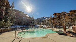 Zona de piscina con cielo despejado, rodeada de edificios y árboles cubiertos de nieve.