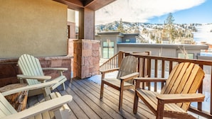 Una terraza de madera con sillas Adirondack, una chimenea de piedra y vistas a un paisaje montañoso nevado.